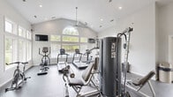 Located at 5300 Catalina Circle Dr in Hilliard, Ohio, this fitness center offers a thoughtfully designed exercise space spread across a single floor. The room is defined by striking vaulted ceilings that rise to an impressive height, creating an open and airy atmosphere. Large, arched windows and an expansive bank of lower windows flood the space with abundant natural light while providing views of the surrounding greenery outdoors. Recessed lighting and two oversized ceiling fans ensure the room remains well-lit and comfortable during workouts.

The exercise area is outfitted with a comprehensive selection of equipment, including multiple treadmills, an elliptical trainer, stationary bikes, and a multi-station cable strength machine. A dedicated stretching and functional fitness zone features stability balls, medicine balls, and a resistance band rack. A wall-mounted mirror expands the sense of space and supports form training. Wall-mounted flat-screen televisions are positioned throughout for entertainment.

The flooring transitions between durable rubber gym matting in the main workout area and hardwood near the entry zone, combining practicality with aesthetic warmth. A wall-mounted water fountain adds everyday convenience. The clean, neutral white walls and high ceilings contribute to a bright, motivating environment well-suited for a full range of fitness activities.