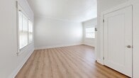 Located just off East Ocean Boulevard in Long Beach, California, this two-bedroom, one-bathroom two-story unit offers a clean, bright, and functional layout spread across two floors. Light wood-look flooring flows consistently throughout the space, creating a warm and cohesive aesthetic from room to room.

The main floor houses two living areas, a kitchen, and a staircase connecting to the upper level. The living room features a ceiling fan with integrated lighting and a charming built-in white dresser unit with glass-panel cabinet doors, adding both storage and character. Natural light enters through white-trimmed windows fitted with blinds. The kitchen is equipped with a gas range, over-the-range microwave, stainless steel refrigerator, white cabinetry, and a small built-in storage cabinet at floor level.

Upstairs, the two bedrooms are well-proportioned and share a clean, minimal design with white walls, crown molding, and windows that bring in natural light. The spacious primary bedroom features dual windows with views of surrounding greenery. The full bathroom includes a tiled tub-shower combination with chrome fixtures and white tile surround, maintaining the home's crisp, clean aesthetic throughout. A hallway connects the upper-level rooms for easy circulation.