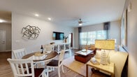 This single-floor residence offers a thoughtfully designed open-concept layout that connects the living, dining, and kitchen areas into one cohesive and functional space. The living area features wood-look flooring, a ceiling fan with integrated lighting, and large windows dressed with curtain panels that invite generous natural light and views of the surrounding greenery. A wall-mounted flat-screen TV sits atop a decorative console, while comfortable seating and layered area rugs contribute to a warm, inviting atmosphere. The adjacent dining space accommodates a round table with white chairs, creating a casual yet refined setting.

The kitchen is well-equipped with dark espresso cabinetry, granite countertops, stainless steel appliances, and a central island with bar-stool seating — ideal for both meal preparation and casual dining. Track lighting overhead adds focused illumination throughout the space.

The bedrooms offer plush carpeting, natural light from well-positioned windows, and walk-in closets with built-in shelving. A bold accent wall in one bedroom adds a distinctive design touch. The bathroom features marble-look tile flooring, a granite vanity, and a glass-enclosed shower, presenting a clean and polished finish throughout.