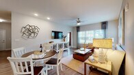 This single-floor residence offers a thoughtfully designed open-concept layout that connects the living, dining, and kitchen areas into one cohesive and functional space. The living area features wood-look flooring, a ceiling fan with integrated lighting, and large windows dressed with curtain panels that invite generous natural light and views of the surrounding greenery. A wall-mounted flat-screen TV sits atop a decorative console, while comfortable seating and layered area rugs contribute to a warm, inviting atmosphere. The adjacent dining space accommodates a round table with white chairs, creating a casual yet refined setting.

The kitchen is well-equipped with dark espresso cabinetry, granite countertops, stainless steel appliances, and a central island with bar-stool seating — ideal for both meal preparation and casual dining. Track lighting overhead adds focused illumination throughout the space.

The bedrooms offer plush carpeting, natural light from well-positioned windows, and walk-in closets with built-in shelving. A bold accent wall in one bedroom adds a distinctive design touch. The bathroom features marble-look tile flooring, a granite vanity, and a glass-enclosed shower, presenting a clean and polished finish throughout.