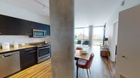 Located at 840 W Blackhawk St in Chicago's vibrant Lincoln Park neighborhood, this contemporary single-floor residence showcases a thoughtfully designed open-concept layout anchored by striking exposed concrete columns and warm hardwood flooring throughout. Floor-to-ceiling glass curtain walls flood the living and dining areas with abundant natural light while framing expansive panoramic views of the Chicago skyline and surrounding cityscape.

The kitchen is outfitted with sleek dark cabinetry, granite countertops, and a full suite of stainless steel appliances including a gas range, built-in microwave, and dishwasher. It connects seamlessly to the dining area and living room, creating an ideal flow for both everyday living and entertaining.

The living room is generously proportioned, featuring a corner arrangement of floor-to-ceiling windows and direct access to a balcony, further extending the indoor-outdoor connection. The bedroom enjoys the same exceptional natural light and city views, with sliding glass balcony access adding an airy, open quality to the private retreat.

The bathroom is cleanly finished with white tile flooring, a dark vanity with granite countertop, and a well-lit mirror above. Throughout the residence, the combination of modern finishes, concrete architectural details, and abundant glazing creates a sophisticated urban aesthetic that is both refined and livable.