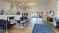 Located at 5300 Glenside Dr in Henrico, Virginia, this single-story community clubhouse offers a thoughtfully designed amenity space that combines modern style with practical functionality. The main lounge is a standout area, boasting soaring ceilings, contemporary sputnik chandeliers, and a sleek fireplace with a wall-mounted television above. Comfortable seating arrangements, hardwood-style flooring, and curated artwork create a warm yet sophisticated atmosphere throughout.

A light-filled café and lounge area features floor-to-ceiling windows that frame views of the outdoor pool, flooding the space with natural light. Mid-century modern dining tables and chairs provide an inviting setting for casual gatherings or quiet relaxation.

The fitness center is well-equipped with treadmills, an elliptical, a rowing machine, and a cable machine, all positioned to take advantage of large windows overlooking the pool area. Adjacent to the gym is a dedicated barre and stretching studio, outfitted with wall-to-wall mirrors and freestanding ballet barres, ideal for group classes or individual workouts.

A stylishly appointed kitchenette rounds out the amenities, featuring powder-blue cabinetry, white subway tile backsplash, a beverage refrigerator, microwave, and a sink — perfect for hosting community events. Throughout the space, cohesive design details and abundant natural light enhance the overall welcoming ambiance.
