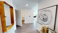 Located at 117 Columbia St NW in Olympia, Washington, this single-floor residence offers a contemporary design defined by clean lines, crisp white walls, and warm wood-tone flooring throughout. The open layout is anchored by expansive floor-to-ceiling windows that flood the interior with natural light and frame remarkable views of Capitol Lake, the surrounding greenery, and the Washington State Capitol dome.

The living area features corner windows on two sides, maximizing panoramic views of both the waterfront and the cityscape. A ceiling fan and recessed lighting provide functional comfort, while the open flow connects seamlessly to the kitchen. The kitchen is outfitted with rich dark cabinetry, a teal herringbone tile backsplash, stainless steel appliances, and a generous island topped with white quartz countertops and pendant lighting above.

The bedroom benefits from large windows offering serene lake views, wood-look flooring, and a stylish light fixture. Two bathrooms are present — each featuring dark wood vanities with light countertops and wood-style flooring. A well-proportioned hallway connects all rooms, accented by recessed lighting and a smart thermostat panel. The overall ambiance is modern, airy, and sophisticated.