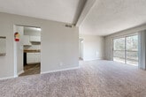 This single-floor, two-bedroom, one-bathroom unit offers a practical and efficient layout across a comfortable footprint. The combined kitchen and living area forms the heart of the unit, with plush carpeting throughout the living space and wood-look flooring in the kitchen. A built-in pass-through shelf connects the living room to the kitchen, adding a convenient architectural detail. The kitchen is equipped with white cabinetry, granite-style laminate countertops, a double stainless steel sink, and black appliances including a range and dishwasher, complemented by an overhead ventilation hood.

The living room is open and versatile, featuring a textured ceiling, neutral beige walls, and a front entry door. Both bedrooms are carpeted and include sliding-door closets, offering adequate storage. The primary bedroom is comfortably sized, while the secondary bedroom provides a similarly functional layout.

The full bathroom features wood-look flooring, white cabinetry with granite-style countertops, a large wall mirror, a single basin sink, and a full tub-shower combination with white tile surround. A hallway connects the main living areas to the bedrooms and bathroom, contributing to the unit's organized flow.