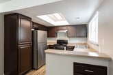 Located at 3940 S 1845 W in West Valley City, Utah, this two-bedroom, one-bathroom single-story home offers a practical and well-organized layout. The open living room is a standout space, featuring rich dark hardwood-style flooring, neutral white walls, a ceiling fan, and a wall-mounted heating unit. A half-wall peninsula with a decorative post separates the living area from the kitchen, adding a subtle architectural detail. The kitchen is equipped with dark cabinetry, a stainless steel dishwasher, and light-toned countertops, providing ample functionality. A connecting hallway leads to the rest of the home, including a dedicated utility room. Both bedrooms are finished with warm, plush carpeting and feature windows with blinds that invite natural light and outdoor views. The primary bedroom is a generously sized retreat, while a walk-in closet with dual hanging rods and carpet flooring offers practical storage. The shared bathroom includes a full tub-shower combination with a curved basin, stainless steel fixtures, and wood-style tile flooring, maintaining a clean and cohesive aesthetic. The home's neutral color palette and consistent finishes create a calm, move-in-ready atmosphere throughout.