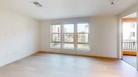 This single-story residence offers 910 square feet of thoughtfully designed living space across three bedrooms and two bathrooms. The open-concept kitchen and living area serves as the home's centerpiece, featuring white shaker cabinetry, a subway tile backsplash, quartz countertops, stainless steel appliances including a French door refrigerator and dishwasher, and a central island illuminated by pendant lighting. Light hardwood flooring runs throughout the kitchen and living areas, contributing to a clean, contemporary aesthetic.

The primary bedroom measures 160 square feet and includes a bank of three large windows providing ample natural light and exterior views of the surrounding community. The two additional bedrooms are finished with neutral carpet and feature windows with outdoor views. One carpeted bedroom includes an electrical panel, indicating a utility function as well.

The two bathrooms reflect a consistent modern finish palette. The primary bathroom features a long vanity with dual sinks, a wide mirror, and a glass-enclosed shower. The second bathroom includes a full tub-shower combination with sliding glass doors and chrome fixtures. Two hallways connect the unit's rooms efficiently, and a dedicated closet provides additional storage.