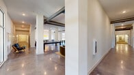 Located at 1191 Lofts Way in Dalton, Georgia, this single-floor amenity space blends industrial-inspired design with contemporary comfort. Polished concrete floors run throughout the main gathering areas, reflecting light and reinforcing the open, loft-style aesthetic. Exposed ductwork traces the ceilings overhead, adding an authentic industrial character that is balanced by crisp white walls and curated artwork displayed throughout the space.

The main social area is expansive and open-plan, with structural columns defining zones without enclosing them. A billiards table anchors one portion of the room, while multiple seating arrangements — including lounge chairs, a sectional sofa, and intimate table groupings — provide flexible settings for socializing or relaxing. A large wall-mounted display serves as a focal point in the lounge area, which is furnished with comfortable upholstered seating and accented by decorative art pieces.

Floor-to-ceiling windows in several areas flood the space with natural light and offer views of the landscaped grounds and surrounding community. The fitness center is well-equipped with cardio machines and strength-training equipment, featuring its own natural light and glass partition walls that maintain visual connectivity to adjacent areas. Overall, the space presents a cohesive, modern environment designed for community engagement and active living.