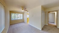 This single-floor residence offers a well-organized layout with a clean, functional design throughout. The living areas are finished with plush, light-toned carpeting that runs consistently through the main rooms, creating a cohesive and comfortable feel underfoot. Warm, neutral-toned walls complement the natural light that filters in generously through multiple large windows fitted with vertical blinds, providing both brightness and privacy.

Each carpeted room is equipped with a ceiling fan featuring a built-in light fixture, ensuring year-round comfort and adequate illumination. The bedrooms include closet storage, with at least one room featuring a built-in closet with sliding doors. Windows in the bedrooms face greenery outdoors, offering pleasant natural views.

The kitchen is compact and efficiently arranged, featuring warm wood-toned cabinetry, a gas range, a full-size refrigerator, and tile flooring. A dark-toned countertop provides practical workspace, and the layout makes efficient use of the available space.

The bathroom is finished with white tile surrounding a full-sized soaking tub and shower combination, complemented by a wood-toned vanity with an integrated sink and a mirrored medicine cabinet above. A window above the tub allows for natural light and ventilation, completing the clean, functional aesthetic found throughout the home.