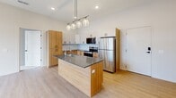 Located at 375 W Whitney Ave in Salt Lake City, UT, this modern single-story home offers three bedrooms, two bathrooms, and a thoughtfully designed layout. The open-concept living, dining, and kitchen area serves as the heart of the home, showcasing a striking contemporary kitchen with a large center island topped with a dark quartz countertop and an integrated sink. Warm natural wood cabinetry on the lower level is paired with crisp white upper cabinets, accented by matte black hardware and a classic white subway tile backsplash. A row of globe pendant lights hangs above the island, adding a stylish focal point. Stainless steel appliances, including a full-size refrigerator, electric range, and microwave, complete the kitchen. Light hardwood-style flooring runs throughout the main living areas, contributing to a bright and airy ambiance. The bedrooms feature plush carpeting and large black-framed windows that bring in natural light. A dedicated pantry, laundry area, and three closets provide ample storage. The bathrooms are clean and functional, with one featuring a full tub-shower combo with white tile surround and oil-rubbed bronze fixtures. This well-appointed home combines modern design with practical living.