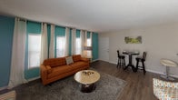 This single-floor residence offers a thoughtfully designed layout that balances comfort and functionality throughout its key living spaces. The open-concept living area features wood-look flooring, a neutral color palette, and large sliding glass doors dressed with vertical blinds that allow natural light to fill the room. A separate sitting area provides additional flexibility, while a compact dining nook with bar-height seating adds a casual touch near the entryway. The galley-style kitchen is efficiently arranged with dark lower cabinetry, white upper cabinets, a double stainless steel sink, laminate countertops, and black appliances, all set atop durable wood-look flooring. A pass-through counter connects the kitchen to the main living space, enhancing the open feel. The bedroom is a standout, featuring a bold teal accent wall that adds vivid character, plush carpeting, a large window with sheer curtains for soft natural light, and ample space for a full furniture suite. The bathroom is clean and practical, with a dark vanity, laminate countertop, a large wall mirror, and brushed nickel fixtures and lighting. Textured ceilings are consistent throughout the residence, contributing to its classic residential character.