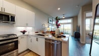 This stylish single-floor residence offers a thoughtfully designed open-concept layout that seamlessly connects the kitchen, dining, and living areas. The contemporary kitchen is a standout feature, showcasing crisp white cabinetry, granite countertops with a herringbone tile backsplash, stainless steel appliances including a gas range, built-in microwave, and dishwasher, along with a peninsula island with an undermount sink — ideal for both cooking and casual entertaining. Wood-look flooring runs throughout the main living areas, enhancing the modern aesthetic.

The living room is bathed in natural light through large sliding glass doors that open to a private balcony, offering pleasant outdoor views. The space is framed by soft neutral walls, a ceiling fan, and generous wall space for art display.

The bedroom is a comfortable retreat, featuring plush carpet, large windows that invite abundant natural light and scenic outdoor views, and ample space for furnishings. Adjacent to the bedroom, the bathroom is finished with large-format tile flooring, a granite-topped vanity with white cabinetry, and a walk-in closet with built-in shelving and hanging storage — providing excellent organization and functionality throughout.