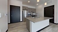 Unit 541 at 808 Melvin Ct is a contemporary 2-bedroom, 2-bathroom apartment spanning 940 square feet on a single floor in Madison, WI. The unit is defined by a clean, modern aesthetic throughout, featuring light wood-style luxury vinyl plank flooring and crisp white walls accented by bold dark door and trim details.

The open-concept living area is bright and airy, benefiting from natural light through a sliding glass door that opens to a private balcony with outdoor views. The kitchen is well-appointed with taupe cabinetry, stainless steel appliances including a refrigerator, range, and microwave, and a center island with a quartz countertop and undermount sink — ideal for both cooking and casual dining.

Both bedrooms offer generous natural light via large windows overlooking the surrounding neighborhood and greenery. The primary bedroom measures 160 square feet. The two bathrooms feature stone-look tile flooring and grey cabinetry with quartz countertops; one bathroom is equipped with accessibility grab bars. A dedicated closet provides additional storage. Throughout the unit, dark-framed doors — including a sleek sliding barn-style door — add a striking architectural contrast to the light, neutral palette.