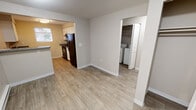 Located at 1790 Sidney Ave in Port Orchard, Washington, this single-floor unit offers a practical and well-organized layout designed for comfortable everyday living. The living area features neutral-toned carpet and is filled with natural light through a sliding glass door that opens to an outdoor space, framed by vertical blinds. The open sightlines create a welcoming atmosphere throughout the main area.

The kitchen is efficiently arranged with white cabinetry, dark speckled countertops, and black appliances, including a refrigerator and range. A window above the counter brings in natural light, enhancing the clean, functional workspace. The kitchen connects openly to the main living space, promoting an easy flow between areas.

A dedicated laundry area is conveniently located off the main hall, housing a full-size washer and dryer alongside a closet for additional storage. The bathroom features wood-look flooring, a dual-sink vanity with dark countertops, a large mirror with overhead lighting, and a tub-shower combination.

Both bedrooms are carpeted and feature baseboard heating, windows with blinds offering views of surrounding greenery, and ample wall space. The neutral color palette throughout the unit contributes to a clean, move-in-ready ambiance.