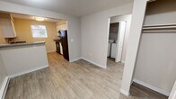 Located at 1790 Sidney Ave in Port Orchard, Washington, this single-floor unit offers a practical and well-organized layout designed for comfortable everyday living. The living area features neutral-toned carpet and is filled with natural light through a sliding glass door that opens to an outdoor space, framed by vertical blinds. The open sightlines create a welcoming atmosphere throughout the main area.

The kitchen is efficiently arranged with white cabinetry, dark speckled countertops, and black appliances, including a refrigerator and range. A window above the counter brings in natural light, enhancing the clean, functional workspace. The kitchen connects openly to the main living space, promoting an easy flow between areas.

A dedicated laundry area is conveniently located off the main hall, housing a full-size washer and dryer alongside a closet for additional storage. The bathroom features wood-look flooring, a dual-sink vanity with dark countertops, a large mirror with overhead lighting, and a tub-shower combination.

Both bedrooms are carpeted and feature baseboard heating, windows with blinds offering views of surrounding greenery, and ample wall space. The neutral color palette throughout the unit contributes to a clean, move-in-ready ambiance.