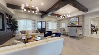 This expansive single-floor community space is thoughtfully designed to balance elegance with functionality. The welcoming entrance features herringbone-patterned tile flooring, exposed dark wood ceiling beams, and striking stacked stone columns flanking a dramatic accent wall, setting the tone for the refined interior throughout.

The central great room serves as the heart of the space, showcasing soaring ceilings adorned with bold dark wood beams and modern sputnik-style chandeliers. Multiple seating arrangements—including cream sofas, navy velvet accent chairs, and patterned wingback seating—are organized around a built-in media wall with dark cabinetry and open shelving. A stacked stone fireplace anchors one end of the room, while large windows flood the space with natural light.

The fully equipped kitchen features dark espresso cabinetry, a dramatic black and gold granite island, stainless steel appliances including double wall ovens, and a subway tile backsplash, making it ideal for hosting and catered events.

A dedicated activity room offers shuffleboard, café-style round tables with upholstered seating, a wall-mounted TV, and its own stone fireplace. The floor plan also reveals a billiards area, providing additional recreational options throughout this well-appointed communal facility.