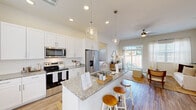 This single-story, 2-bedroom, 2-bathroom home offers a thoughtfully designed open-concept layout that maximizes both functionality and comfort. The kitchen serves as the heart of the home, showcasing white shaker cabinetry, granite countertops, stainless steel appliances, and a central island with bar seating illuminated by elegant glass pendant lights. The kitchen flows seamlessly into the dining and living areas, where wood-look flooring, a ceiling fan, and a sliding glass door leading to a private outdoor patio create a bright and airy atmosphere. The primary bedroom is a comfortable retreat featuring tall windows that invite natural light, a ceiling fan, and a dedicated closet. Its en-suite bathroom includes a glass-enclosed walk-in shower, granite vanity, and wood-look tile flooring. The second bedroom mirrors the same warm, neutral aesthetic with its own closet and ample natural light. The second bathroom offers a shower-tub combination with a granite vanity. A flexible dining room with natural light and built-in cabinetry provides additional versatile space. A dedicated closet and hallways complete the floor plan. Throughout the home, neutral tones, consistent finishes, and clean architectural lines create a cohesive and inviting environment.