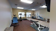 This fitness center offers a comprehensive workout environment designed to support a variety of exercise routines. The space is outfitted with multiple cardio machines, including treadmills, a stair climber, and a stationary bike, providing ample options for cardiovascular training. A dedicated free weights area features a dumbbell rack and a weight bench, catering to strength training needs. An ab workout machine rounds out the available equipment, ensuring a full-body fitness experience. A full-length wall mirror spans one side of the room, enhancing the sense of space while allowing users to monitor their form during workouts. The room is illuminated by recessed fluorescent ceiling fixtures and benefits from natural light streaming through several windows fitted with blinds. The flooring combines dark carpet and rubber exercise mats in the weight area, providing both comfort and functionality. The walls are finished in a neutral, warm tone, contributing to a clean and focused atmosphere. With its thoughtful layout and variety of equipment, this fitness center is well-suited to meet the everyday workout needs of its users.