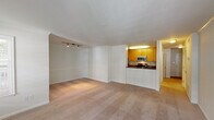 This single-floor residence offers a well-organized layout with clearly defined living, sleeping, and functional zones. The open living and dining area is expansive, finished with neutral-toned wall-to-wall carpeting and crisp white walls that create a bright, clean atmosphere. Track lighting accents one section of the living space, while multiple windows admit natural light throughout. A pass-through counter with a dark granite-style surface connects the living area to the kitchen, providing both a visual boundary and a convenient serving surface.

The galley kitchen features warm honey-toned cabinetry paired with dark granite-style countertops on both sides. Stainless steel appliances include an electric range, over-the-range microwave, and refrigerator, complemented by a stainless sink. Light hardwood flooring runs through the kitchen, adding warmth and contrast to the cabinetry.

The bedrooms are carpeted and generously sized, each receiving natural light through sizable windows with blinds. One bedroom includes a ceiling fan with integrated lighting. Both bathrooms share a consistent design language: warm wood vanities, dark countertops, tiled tub-shower combinations, and light tile flooring, offering a cohesive and functional finish throughout.
