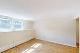 Located at 2 Lincoln St in Milford, MA, this two-bedroom, one-bathroom single-floor unit offers a practical and well-organized layout. Light-toned hardwood flooring runs throughout the living areas and bedrooms, lending warmth and continuity to the space. The living room provides a comfortable gathering area, while the combined dining and kitchen space is efficiently designed with white shaker cabinetry, granite-look countertops, white appliances including a range and refrigerator, and light tile flooring. Natural light filters in through multiple windows, giving the kitchen and dining area a bright, airy feel. Both bedrooms are finished with the same warm hardwood floors and cream-toned walls, with multiple windows offering natural light and outdoor views of surrounding greenery. The primary bedroom includes a built-in shelf nook, adding functional character. Five closets distributed throughout the unit provide generous storage. The bathroom features a full tub and shower combination with white tile surround, chrome fixtures, and a window for ventilation. Baseboard heating is present throughout. With two entrance points and a central hallway connecting the rooms, the layout is both functional and easy to navigate.