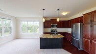 This single-floor residence offers a thoughtfully designed layout that balances functionality and comfort throughout its living spaces. The kitchen serves as a central highlight, showcasing rich dark cherry wood cabinetry, a granite-topped island with a built-in sink and dark panel base, and a full suite of stainless steel appliances including a refrigerator, range, and over-the-range microwave. Pendant lighting above the island and a large window overlooking greenery fill the kitchen with natural light and warmth. The adjacent living area features plush neutral carpeting and an open, airy feel.

The bedrooms are carpeted and bright, each benefiting from well-sized windows that bring in natural light and offer views of the surrounding landscape. The primary bedroom area provides access to a dedicated bathroom featuring a double-sink vanity with a white countertop, rich wood cabinetry, and a large framed mirror with overhead lighting. A secondary full bathroom includes a tub-shower combination, dark wood vanity, and hardwood-style flooring. Throughout the home, neutral wall tones, clean white trim, and consistent finishes create a cohesive and inviting atmosphere.