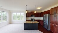 This single-floor residence offers a thoughtfully designed layout that balances functionality and comfort throughout its living spaces. The kitchen serves as a central highlight, showcasing rich dark cherry wood cabinetry, a granite-topped island with a built-in sink and dark panel base, and a full suite of stainless steel appliances including a refrigerator, range, and over-the-range microwave. Pendant lighting above the island and a large window overlooking greenery fill the kitchen with natural light and warmth. The adjacent living area features plush neutral carpeting and an open, airy feel.

The bedrooms are carpeted and bright, each benefiting from well-sized windows that bring in natural light and offer views of the surrounding landscape. The primary bedroom area provides access to a dedicated bathroom featuring a double-sink vanity with a white countertop, rich wood cabinetry, and a large framed mirror with overhead lighting. A secondary full bathroom includes a tub-shower combination, dark wood vanity, and hardwood-style flooring. Throughout the home, neutral wall tones, clean white trim, and consistent finishes create a cohesive and inviting atmosphere.
