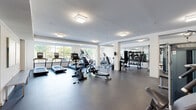 Located at 4225 Innslake Dr in Glen Allen, Virginia, this fitness center offers a well-appointed, single-floor exercise facility designed to support a full range of workout routines. The space is generously sized, providing ample room for both cardio and strength training without feeling crowded.

The cardio zone is anchored by a row of Matrix treadmills positioned along large windows that usher in natural light and offer views of the surrounding greenery — creating an energizing environment for endurance training. Alongside the treadmills, users will find elliptical machines, stationary bikes, and rowing machines to diversify their cardio sessions.

The strength training area is equally well-equipped, featuring multiple Matrix cable and weight machines set against a striking natural wood accent wall that adds warmth and texture to the otherwise clean, modern interior. A dedicated free weights section includes a full dumbbell rack with mirror backing, benches, and additional resistance equipment.

The flooring throughout is durable rubber — practical and supportive underfoot. Overhead, modern flush-mount lighting ensures the entire space is evenly and brightly lit. Colorful abstract artwork adorns one wall, contributing a polished, welcoming aesthetic. Glass-panel entry doors and a bench along the perimeter round out the functional design of this comprehensive fitness facility.