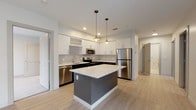 Located at 200 Presidential in Woburn, MA, this single-floor residence offers a thoughtfully designed layout with modern finishes and an open, airy atmosphere. The kitchen is a standout feature, showcasing two-tone cabinetry with white upper cabinets and dark lower cabinets, light-toned granite countertops, a tile backsplash, and a central island with pendant lighting overhead. Stainless steel appliances, including a refrigerator, range, microwave, and dishwasher, complete the sleek culinary space. Light wood-style flooring flows seamlessly through the kitchen and into the open living area, which is bathed in natural light through large windows with roller shades and a sliding glass door that opens to an outdoor balcony with wooded views. A carpeted bedroom also enjoys direct access to the balcony via its own floor-to-ceiling slider, framing peaceful natural scenery. The residence includes two bathrooms: a primary bath featuring a wood-toned vanity, white countertop, large-format tile flooring, and a glass-enclosed walk-in shower; and a second bathroom with a clean, all-white aesthetic and a soaking tub with shower combination. The overall design is clean, contemporary, and inviting throughout.