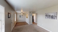 This single-floor residence offers a well-organized layout with a functional flow between its main living spaces. The open living and dining area serves as the heart of the home, featuring a combination of hardwood-style flooring and plush carpeting that delineates distinct zones. A ceiling fan with a light fixture provides both comfort and overhead illumination, while a window along the front wall allows natural light to fill the space. A pass-through opening connects the living area directly to the kitchen, enhancing the open feel.

The galley-style kitchen is efficiently designed with white cabinetry, light countertops, a double basin sink, and black appliances including a range and refrigerator. Hardwood-style flooring and track lighting overhead give the kitchen a clean, practical character.

The two bedrooms are carpeted and finished in warm neutral tones, each featuring ceiling fans and windows with blinds that provide natural light. Both rooms offer a comfortable sense of space with clean, simple finishes.

The bathroom includes a tub and shower combination with terracotta-toned tile surround, complemented by neutral wall tones. The overall ambiance of the unit is understated and move-in ready, with consistent neutral tones and functional finishes throughout.