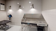 Located at 4701 Forest Dr in Forest Acres, SC, this single-floor professional pet grooming facility is designed with both functionality and charm in mind. The grooming room is the heart of the space, finished with crisp white subway tile wainscoting that lines the lower portion of the walls, creating a hygienic and easy-to-clean surface. The upper walls are painted in a soft, neutral gray tone, lending the space a clean and calm atmosphere.

The room is equipped with a professional-grade stainless steel bathing tub, complete with plumbing fixtures and a spray hose, illuminated by a pair of brushed nickel wall sconces that provide focused task lighting. A grooming table with a padded, non-slip surface sits nearby, offering a dedicated area for post-bath grooming and styling. The floors are finished in a smooth, high-gloss white coating that is both practical and visually bright.

Adding personality and warmth to the otherwise clinical environment, a series of vibrant, large-format framed artworks featuring colorful painted portraits of various dog breeds — including a Pomeranian, Chihuahua, Schnauzer, and Maltese — are displayed prominently along one wall. Recessed ceiling lighting ensures the entire space is evenly and brightly lit. A fire alarm and coded access door round out the room's safety and security features.