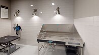Located at 4701 Forest Dr in Forest Acres, SC, this single-floor professional pet grooming facility is designed with both functionality and charm in mind. The grooming room is the heart of the space, finished with crisp white subway tile wainscoting that lines the lower portion of the walls, creating a hygienic and easy-to-clean surface. The upper walls are painted in a soft, neutral gray tone, lending the space a clean and calm atmosphere.

The room is equipped with a professional-grade stainless steel bathing tub, complete with plumbing fixtures and a spray hose, illuminated by a pair of brushed nickel wall sconces that provide focused task lighting. A grooming table with a padded, non-slip surface sits nearby, offering a dedicated area for post-bath grooming and styling. The floors are finished in a smooth, high-gloss white coating that is both practical and visually bright.

Adding personality and warmth to the otherwise clinical environment, a series of vibrant, large-format framed artworks featuring colorful painted portraits of various dog breeds — including a Pomeranian, Chihuahua, Schnauzer, and Maltese — are displayed prominently along one wall. Recessed ceiling lighting ensures the entire space is evenly and brightly lit. A fire alarm and coded access door round out the room's safety and security features.