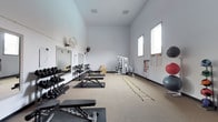 Located at 8504 82nd St SW in Tacoma, Washington, this single-floor fitness facility is purpose-built to support a comprehensive range of training activities. The space features impressively high ceilings that create an open, airy atmosphere, allowing for unrestricted movement and a sense of spaciousness throughout the workout area. The walls are finished in a clean, neutral white, and the flooring consists of a durable carpet tile surface with rubber mat stations positioned at key training areas.

Along the left wall, a full rack of dumbbells spans a wide range of weights, accompanied by multiple adjustable weight benches ideal for strength training. Large mirrors are mounted nearby, allowing athletes to monitor their form during lifts. Wall-mounted fans provide ventilation throughout the space.

The central floor area offers open room for functional movement, agility ladder drills, and floor-based exercises. A multi-station cable machine anchors the far end of the room, providing a versatile option for resistance training. To the right, resistance bands, exercise charts, and a collection of stability balls round out the facility's equipment offerings.

Natural light filters in through high windows along the right wall, enhancing the bright and motivating training environment. This facility is well-suited for personal training, athletic conditioning, and general fitness use.