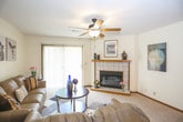 This single-floor residence offers a practical and comfortable layout across several well-defined living spaces. The living room serves as the heart of the home, anchored by a tile-surround fireplace with a warm wood mantel and equipped with a ceiling fan. A sliding glass door floods the space with natural light and provides direct access to an outdoor balcony, offering pleasant views of surrounding greenery. The living area flows naturally into a dedicated dining space, illuminated by track lighting overhead, with neutral carpet throughout creating a cohesive, understated aesthetic. Textured ceilings are consistent throughout the unit.

The kitchen features solid oak cabinetry with ample storage, gray laminate countertops, a double-basin sink, and tile flooring. It is equipped with a full suite of appliances including an electric range and dishwasher.

Two bedrooms provide comfortable accommodations, each carpeted and fitted with windows that invite natural light. Both rooms offer adequate space for standard bedroom furniture, and the primary bedroom is notably larger with additional room for a nightstand and dresser.

The full bathroom includes a tub-shower combination, a wood-trimmed vanity with integrated sink, and tile flooring, completing this well-organized and functional residence.
