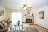 This single-floor residence offers a practical and comfortable layout across several well-defined living spaces. The living room serves as the heart of the home, anchored by a tile-surround fireplace with a warm wood mantel and equipped with a ceiling fan. A sliding glass door floods the space with natural light and provides direct access to an outdoor balcony, offering pleasant views of surrounding greenery. The living area flows naturally into a dedicated dining space, illuminated by track lighting overhead, with neutral carpet throughout creating a cohesive, understated aesthetic. Textured ceilings are consistent throughout the unit.

The kitchen features solid oak cabinetry with ample storage, gray laminate countertops, a double-basin sink, and tile flooring. It is equipped with a full suite of appliances including an electric range and dishwasher.

Two bedrooms provide comfortable accommodations, each carpeted and fitted with windows that invite natural light. Both rooms offer adequate space for standard bedroom furniture, and the primary bedroom is notably larger with additional room for a nightstand and dresser.

The full bathroom includes a tub-shower combination, a wood-trimmed vanity with integrated sink, and tile flooring, completing this well-organized and functional residence.