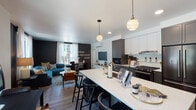 Located at 4103 Mercantile Dr in Lake Oswego, Oregon, this single-floor residence combines contemporary design with functional living across a well-planned layout. The entryway welcomes residents with clean white walls, wall-mounted hooks for everyday storage, and light hardwood flooring that carries throughout the unit.

The open-concept kitchen is a standout feature, showcasing two-tone cabinetry in white and dark gray with brass hardware, a gas range with a stainless steel hood, a dark French-door refrigerator, and quartz countertops. A large island with seating serves as both a workspace and gathering hub, illuminated by globe pendant lights. Herringbone-patterned hardwood flooring adds a sophisticated touch underfoot.

The living area offers generous space with a bold dark accent wall, large windows admitting ample natural light, a wall-mounted mini-split system, and a built-in media console. Bedrooms feature large windows with outdoor views, dark accent walls, and mini-split units for individual climate control.

Two bathrooms display refined finishes, including dark cabinetry, white quartz vanities, and walk-in shower and tub options. Throughout, the home balances bold, moody accents with bright, airy spaces for a cohesive modern aesthetic.