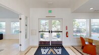 Located at Cobble Creek Circle in Rocklin, California, this single-story leasing office and clubhouse serves as the central hub for AVA Apartments. The entrance greets visitors with a clean, modern lobby framed by glass double doors that flood the space with natural light and offer views of the surrounding community. Light-toned tile flooring runs throughout, complementing the crisp white walls and creating a bright, cohesive aesthetic.

The main lounge area is expansive and versatile, anchored by soaring vaulted ceilings that enhance the sense of openness. This social hub features comfortable seating arrangements, a large flat-screen television, and a foosball table, making it an ideal space for residents to gather and relax. Multiple windows along the perimeter bring in abundant natural light and provide views of the lush greenery outside.

Adjacent to the lounge is a dedicated meeting and work area distinguished by a bold dark accent wall that adds a modern, design-forward touch. This room is equipped with a natural wood table and stylish cane-back chairs, creating a functional yet inviting setting for residents to work or meet. Windows on multiple walls ensure this room remains well-lit throughout the day. Together, these areas form a well-appointed community space designed for both productivity and leisure.