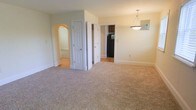 Located at 210 C, this single-floor space offers a practical and comfortable layout with a cohesive design throughout. The main living area is finished with plush neutral-toned carpeting that adds warmth underfoot and flows seamlessly through the space. Soft, light green walls create a calm and welcoming ambiance, complemented by clean white trim and baseboards that frame each room neatly.

A distinctive arched passageway on one side of the living area adds an architectural touch, leading into an adjoining carpeted room that provides additional living space. A standard hinged door nearby opens to what appears to be a closet or utility area, offering convenient built-in storage. On the opposite side, an open doorway provides a direct sightline into the kitchen, where dark cabinetry and a black refrigerator are visible, hinting at a well-equipped cooking space.

A pendant light fixture hangs in the dining area, providing focused overhead lighting and serving as a subtle design accent. The overall layout feels open and connected, with clearly defined zones for living, dining, and access to other areas of the unit, making the space functional and easy to navigate.