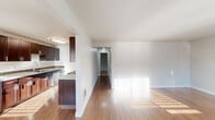 This single-floor residence offers a practical and comfortable layout across two bedrooms, one bathroom, and a combined living and dining area. The living room serves as the heart of the home, highlighted by a fireplace with a white mantel surround and a large window fitted with horizontal blinds that invites generous natural light. Warm hardwood-style flooring extends throughout the main living areas, reflecting sunlight and adding a sense of warmth to the space.

The galley-style kitchen is well-equipped, featuring rich dark-stained cabinetry reaching toward the ceiling, stone-accented tile backsplash, light countertops, and stainless steel appliances including a range and dishwasher. A half-wall separates the kitchen from the open living and dining area, creating a connected yet defined flow between spaces.

Both bedrooms offer a quieter retreat, finished with plush neutral carpet and windows providing outdoor views. The primary bedroom is a comfortable size, while the secondary bedroom also benefits from natural light. The bathroom is cleanly appointed with dark wood vanity cabinetry, a white countertop, a combined tub and shower with grab bars, built-in storage, and hardwood-style flooring. A hallway connects the private areas of the home to the main living space.