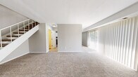 This two-floor residence offers a well-designed layout with a consistent neutral color palette of soft grays and whites throughout. The main level features a spacious living area with plush beige carpeting, light-filled by a large sliding door dressed with vertical blinds that allow ample natural light. A staircase with white railings connects the two floors and adds a clean architectural element to the space.

The kitchen is a standout feature, showcasing white shaker-style cabinetry paired with granite countertops, a gray subway tile backsplash, and stainless steel appliances including a range, dishwasher, and refrigerator. Light wood-look flooring ties the kitchen together, and a peninsula with additional cabinetry opens toward the living area, creating a functional and connected layout.

A bathroom on the upper level includes a white vanity with granite countertops, a large mirror, and a well-lit vanity fixture above, complemented by wood-look flooring.

The bedrooms are carpeted and generously sized, each featuring vertical blinds over sliding doors and closets with built-in shelving and hanging rods. Throughout the home, clean white trim and subdued wall tones create a cohesive, move-in-ready atmosphere.