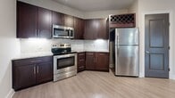 Located at 13504 Citicards Way in Jacksonville, FL, this well-appointed 840-square-foot, single-story apartment offers 1 bedroom and 1 bathroom with a thoughtfully designed layout. The open-concept living room and kitchen area is finished with light wood-style flooring, neutral beige walls, and a ceiling fan, with natural light flowing in through windows fitted with blinds. The kitchen is a standout feature, boasting rich dark-espresso cabinetry, granite countertops, a marble-style tile backsplash, a kitchen island, and a full suite of stainless steel appliances including a range, microwave, and refrigerator, plus a built-in wine rack. The 170-square-foot primary bedroom is carpeted for comfort, includes a ceiling fan, and provides direct access to both the bathroom and a spacious walk-in closet outfitted with wire shelving and carpet flooring. The bathroom features a dark wood vanity with granite countertop, a tub/shower combination with marble-style tile surround, and wood-look flooring. A dedicated in-unit laundry area accommodates a full-size washer and dryer. The unit's consistent use of dark door hardware and rich cabinetry tones throughout creates a cohesive, modern aesthetic.