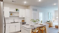 Located at 3100 Ascend Loop in Leland, NC, this thoughtfully designed 2-bedroom, 2-bathroom residence offers a comfortable and cohesive single-level layout. The open-concept living and kitchen area serves as the heart of the home, featuring light hardwood-style flooring, a ceiling fan, and large windows dressed with bright curtains that invite abundant natural light. A glass door provides direct outdoor access from the living area. The kitchen is outfitted with white shaker cabinetry, a classic subway tile backsplash, granite countertops, stainless steel appliances, and a central island with seating — ideal for both cooking and casual dining. The primary bedroom is a calm, well-lit retreat with dual windows, plush carpeting, and a dedicated en-suite bathroom. The en-suite features granite countertops, white cabinetry, a large mirror, and access to a walk-in closet with built-in shelving. The second bedroom mirrors the serene aesthetic with natural light, a ceiling fan, and carpeted flooring. A second full bathroom maintains the same clean, modern design with granite vanity surfaces and white cabinetry. A hallway and closet complete the functional layout of this well-designed Leland residence.