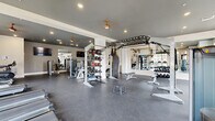 Located in Huntersville, NC, this well-equipped fitness center offers a generous, open single-floor layout designed to accommodate a full spectrum of workout styles. The space is finished with durable rubber flooring throughout, providing a safe and functional surface for all types of exercise. Large windows along multiple walls flood the interior with natural light, creating an energizing atmosphere while offering pleasant outdoor views. Recessed lighting and ceiling fans complement the bright, airy environment.

The strength training area is extensively equipped with a multi-station functional rig featuring TRX suspension trainers and a heavy bag, a full rack of dumbbells, barbells with weight plates, multiple adjustable benches, and a variety of selectorized cable machines. A dedicated storage rack holds an assortment of medicine balls and kettlebells, supporting dynamic and functional fitness routines.

The cardio zone features a row of treadmills and step machines positioned near the windows, maximizing natural light during workouts. Wall-mounted mirrors and flat-screen TVs are strategically placed throughout, enhancing both the visual spaciousness and the overall workout experience. The clean, neutral color palette of white walls and gray accents lends the facility a modern, professional aesthetic well-suited for serious fitness pursuits.