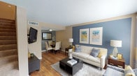 This two-floor residence offers a thoughtfully designed layout with comfortable living spaces spread across both levels. The main floor opens into a bright living room highlighted by a striking blue accent wall adorned with framed artwork, warm hardwood flooring, and a large window that invites natural light. The living area flows seamlessly into a dedicated dining space with a circular table and a wall-mounted mirror, creating an inviting atmosphere for entertaining. Adjacent to the dining area is a casual breakfast nook with tile flooring and a sliding glass door that opens to the outdoors. The kitchen is well-appointed with white cabinetry, granite-style countertops, stainless steel appliances including a range, microwave, and refrigerator, and tile flooring throughout. A convenient half bath with a granite vanity and tile flooring is tucked beneath the staircase on the main level. Upstairs, two carpeted bedrooms each feature ceiling fans, closets with bifold doors, and accent walls in warm earth tones and cool gray respectively. A full bathroom with a granite vanity and a tub-shower combination serves the upper level. The overall aesthetic balances neutral tones with coordinated accent colors, creating a cohesive and welcoming environment throughout.