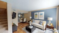 This two-floor residence offers a thoughtfully designed layout with comfortable living spaces spread across both levels. The main floor opens into a bright living room highlighted by a striking blue accent wall adorned with framed artwork, warm hardwood flooring, and a large window that invites natural light. The living area flows seamlessly into a dedicated dining space with a circular table and a wall-mounted mirror, creating an inviting atmosphere for entertaining. Adjacent to the dining area is a casual breakfast nook with tile flooring and a sliding glass door that opens to the outdoors. The kitchen is well-appointed with white cabinetry, granite-style countertops, stainless steel appliances including a range, microwave, and refrigerator, and tile flooring throughout. A convenient half bath with a granite vanity and tile flooring is tucked beneath the staircase on the main level. Upstairs, two carpeted bedrooms each feature ceiling fans, closets with bifold doors, and accent walls in warm earth tones and cool gray respectively. A full bathroom with a granite vanity and a tub-shower combination serves the upper level. The overall aesthetic balances neutral tones with coordinated accent colors, creating a cohesive and welcoming environment throughout.