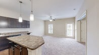 Located at 1000 Channel Marker Way in Hanahan, South Carolina, this one-bedroom, one-bathroom residence offers a well-organized single-floor layout designed for comfortable everyday living. The open-concept living and kitchen area is the heart of the home, where rich dark espresso cabinetry pairs with granite-style countertops and a peninsula breakfast bar illuminated by stylish pendant lights. Black appliances, including a refrigerator, range, and over-the-range microwave, complete the kitchen, which features wood-look flooring for easy maintenance. The living area transitions seamlessly from the kitchen, highlighted by plush carpeting, a ceiling fan with light fixture, and a private exterior door that brings in natural light. The bedroom is a cozy, carpeted retreat with a window offering neighborhood views, a ceiling fan, and a dedicated closet for storage. The bathroom is neatly appointed with a dark vanity complementing granite-style counters, a single sink, a tub-shower combination, and wood-look flooring that ties the space together. Neutral wall tones throughout create a clean, versatile backdrop, while the overall layout makes efficient use of every square foot in this Hanahan residence.