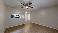 Located at 5900 Wurzbach Road in Leon Valley, TX, this single-story, 2-bedroom, 1-bathroom unit offers a well-organized and functional layout. The open living area features warm wood-look laminate flooring and a ceiling fan with light, creating a bright and comfortable atmosphere. A pass-through window connects the living space to the kitchen, enhancing the open feel. The galley-style kitchen is efficiently designed with white cabinetry, granite-look countertops, a tile backsplash, and black appliances including an electric range, dishwasher, and refrigerator. Both bedrooms are equipped with ceiling fans and closets — one featuring a sliding-door closet — providing practical storage solutions. Natural light enters through blinds-covered windows, complementing the neutral gray walls throughout. The full bathroom includes a vanity with white cabinetry, a tiled shower-tub combo, and wood-look flooring. A hallway connects the main living areas to the bedrooms and bathroom, with multiple additional closets offering generous storage. The textured ceilings add a classic touch consistent throughout the home. The unit provides a clean, move-in-ready environment suited for comfortable everyday living.