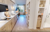 This efficiently designed 300-square-foot, one-bedroom, one-bathroom residence maximizes every inch of its single-floor layout with a clean, modern aesthetic. Light hardwood flooring and bright white walls run throughout, creating a cohesive and airy atmosphere.

The galley-style kitchen is well-equipped, featuring light wood cabinetry with brushed metal hardware, white quartz countertops, a stainless steel double sink, an induction cooktop, a built-in microwave, a full-size bottom-freezer refrigerator, and a dishwasher. Open shelving adds display and storage space. A stacked washer and dryer unit is conveniently integrated into the kitchen corridor, eliminating the need for a separate laundry room.

The primary bedroom measures 160 square feet and offers a natural window view of outdoor greenery, flooding the room with natural light. A wall-mounted TV, a dedicated workspace area, and a sliding-door closet provide practical functionality. The bedroom also features a wall-mounted mini-split HVAC system for individual climate control, and a textured brick accent wall adds architectural character.

The bathroom is clean and minimal, with light wood built-in shelving, a glass-enclosed walk-in shower, and light wood-tone flooring. The overall design of this unit prioritizes smart use of space, modern finishes, and functional living.