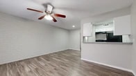 Located at 403 Small Hill Dr in Grand Prairie, Texas, this single-floor unit offers a well-organized layout across three distinct areas. The main living space is a standout, featuring a striking whitewashed brick accent wall that adds texture and character to the room. Wood-look vinyl plank flooring runs throughout, providing a cohesive and easy-to-maintain surface. A ceiling fan with an integrated light fixture centers the living area, ensuring both comfort and illumination. Recessed lighting further brightens the space.

The kitchen is accessed via a passthrough opening from the living area, creating an open and connected feel. It is designed in a galley style, equipped with white cabinetry, gray laminate countertops, and black appliances including a refrigerator and range. Open shelving provides additional storage alongside the cabinetry.

The bathroom features tile flooring, a white vanity with gray countertop, and a full tub and shower combination enclosed in warm-toned tile with a decorative mosaic accent border. The entry area provides a clean and simple transition into the home through a solid white panel door. Overall, the unit presents a clean, neutral palette throughout, making it a versatile and functional living space.