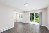 This single-floor unit is designed with a practical, open layout that connects its key living spaces efficiently. The living area serves as the heart of the unit, finished with smooth hardwood-style flooring and neutral beige walls that create a clean, inviting atmosphere. A sliding glass door floods the space with natural light and opens directly to a patio overlooking a green lawn, while an additional side window enhances ventilation and brightness. Baseboard heating is present throughout, ensuring year-round comfort.

The galley-style kitchen is well-appointed with white shaker cabinetry extending to the ceiling, dark countertops, a stainless steel sink, and appliances including a stainless refrigerator, microwave, and white electric range. Track lighting overhead ensures functional illumination across the workspace.

The bedroom features plush carpeting, neutral walls, a sliding double-door closet providing ample storage, and a window with blinds for natural light. An adjacent area with hardwood-style flooring and a closet offers flexible use as a secondary bedroom or den.

The bathroom is finished with hardwood-style flooring, a white vanity with dark countertop, and a full tub-shower combination, completing this well-maintained and thoughtfully designed space.