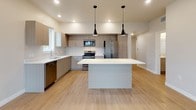 This single-floor residence presents a clean, contemporary design characterized by light wood-style flooring, neutral tones, and recessed lighting throughout. The open-concept kitchen serves as a central highlight, featuring flat-front cabinetry in a warm gray finish, white quartz countertops, and a full suite of stainless steel appliances including a refrigerator, electric range, built-in microwave, and dishwasher. A generously sized center island with pendant lighting overhead provides additional prep space and casual seating, while a window above the sink introduces natural light into the workspace.

The living area offers an open, airy feel with smooth ceilings and large sliding glass doors that connect the interior to a private balcony, providing views of the surrounding urban streetscape and filling the space with natural light. The layout flows efficiently between the living and kitchen areas, as illustrated by the dollhouse floor plan view.

The bathroom is outfitted with a full tub-shower combination featuring white tile surround, chrome fixtures, a toilet, and a vanity with light wood cabinetry and a white countertop. The same light wood flooring carries throughout, creating a cohesive and unified aesthetic across the entire unit. Overall, the space offers a well-appointed, move-in-ready environment with modern finishes.