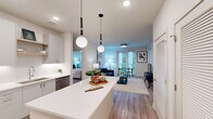 Located at 222 N West St in the heart of downtown Raleigh, NC, this thoughtfully designed 2-bedroom, 2-bathroom residence offers a clean, contemporary aesthetic throughout. The open-concept living area seamlessly connects the kitchen, dining, and living spaces, all finished with warm wood-look flooring and crisp white walls. The modern kitchen is a standout feature, boasting a large center island with quartz countertops, white cabinetry, stainless steel appliances, and globe pendant lighting that adds a stylish focal point. The living and dining area is bathed in natural light from full-length windows and a glass door leading to a private balcony. Both bedrooms are well-appointed, featuring ceiling fans, large windows, and generous closet space. The primary suite includes a spacious walk-in closet with custom built-in shelving and drawers. The en-suite bathroom offers a dual-sink vanity with a backlit mirror and a glass-enclosed tile shower. The second bathroom mirrors the same refined finishes. Additional highlights include multiple closets, a dedicated laundry area, and a utility room, ensuring ample storage throughout. The overall ambiance is light, airy, and move-in ready.